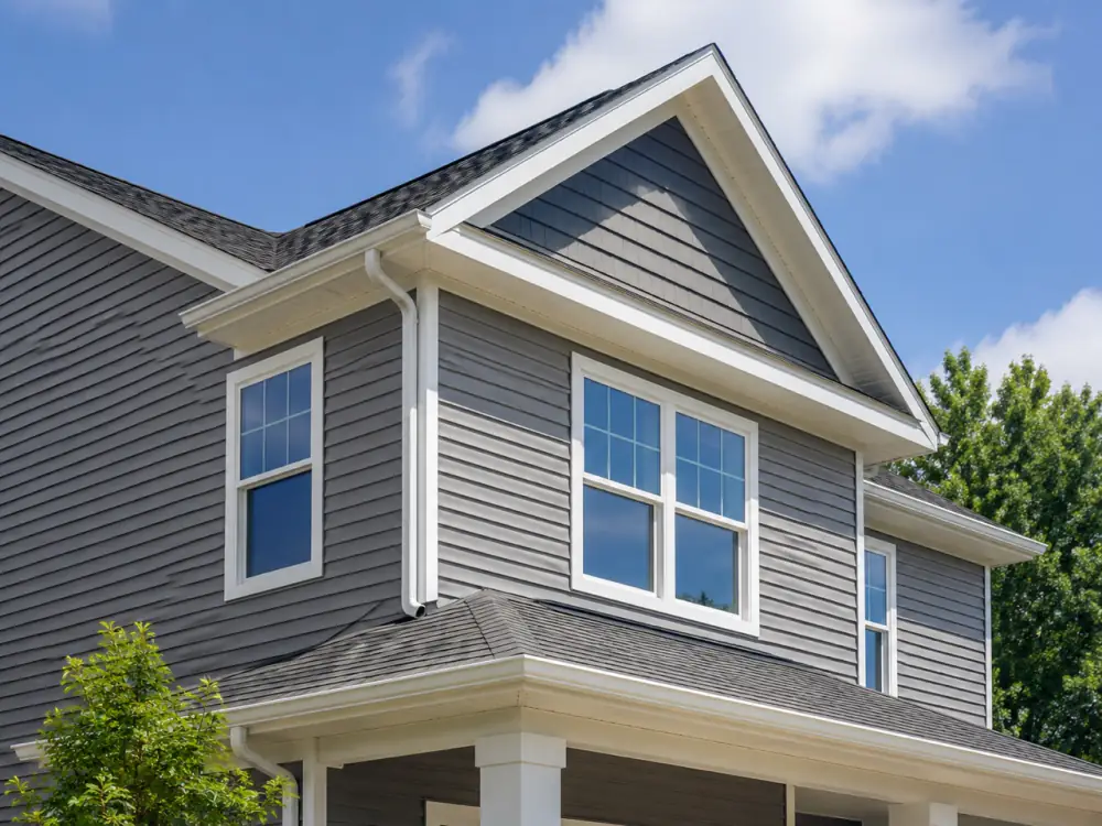 Two-storey house corner with grey horizontal siding, shake-style gable accents and white-trimmed windows